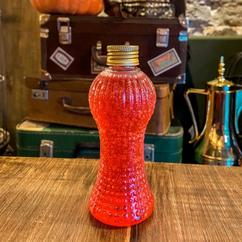 Uma garrafinha transparente com líquido vermelho e tampa dourada
