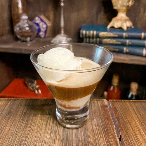 Uma taça transparente com sorvete e espresso. Ao fundo, uma prateleira com diversos itens coloridos.