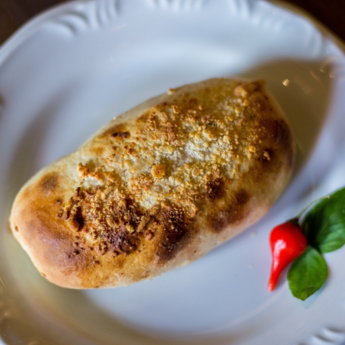 Uma baguete coberta por queijo ralado tostadinho, em um prato branco