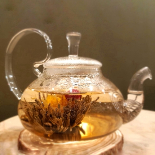 Um bule grande com uma flor de chá, já aberta, dentro.