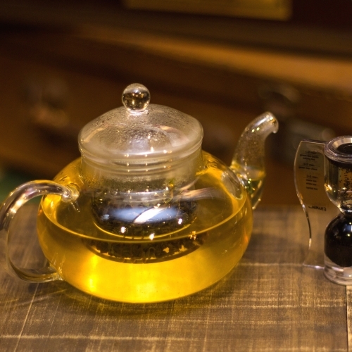 Um bule de chá com cor clara e uma ampulheta ao lado