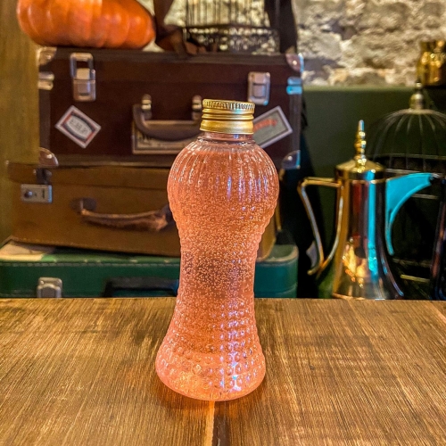 Uma garrafinha transparente com líquido rosa e tampa dourada