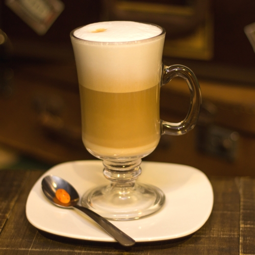 Uma caneca transparente exibindo a crema do leite, o café e o leite em camadas