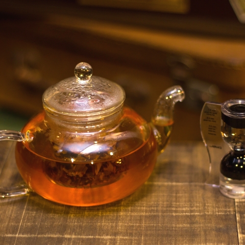 Um bule de chá com uma cor avermelhada e uma ampulheta ao lado