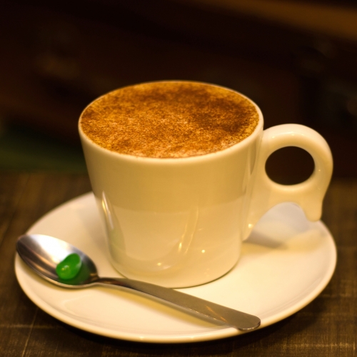 Uma xícara branca com café e leite, coberta por canela e chocolate em pó