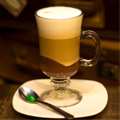 Uma caneca transparente exibindo a crema do leite, o café, o leite e o ganache de chocolate em camadas