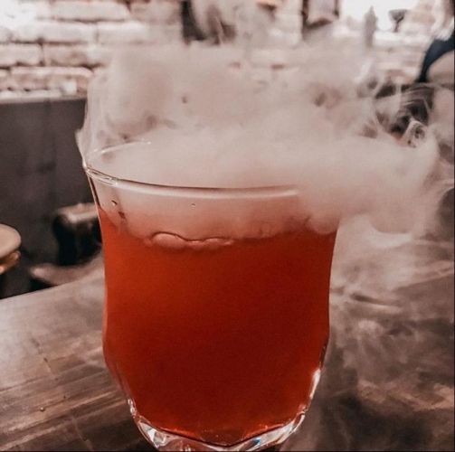 Um copo transparente com líquido vermelho e fumaça branca saindo por cima.